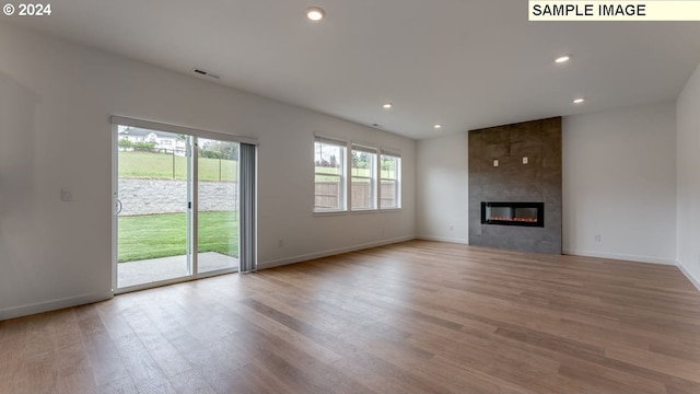 unfurnished living room with recessed lighting, visible vents, wood finished floors, a tile fireplace, and baseboards