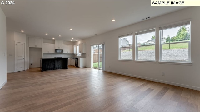 kitchen with visible vents, stainless steel microwave, open floor plan, light wood-type flooring, and white cabinetry