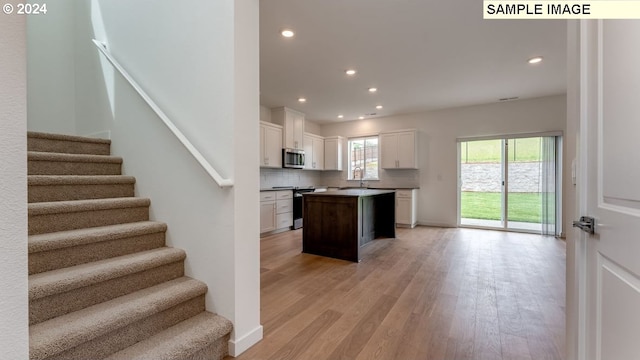 kitchen with stainless steel appliances, a kitchen island, white cabinets, light wood-style floors, and tasteful backsplash