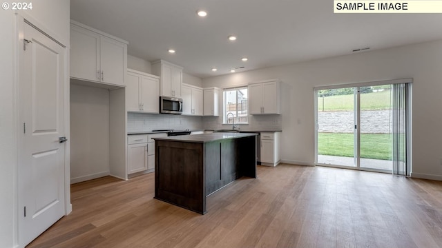 kitchen featuring stainless steel microwave, light wood-type flooring, a sink, and decorative backsplash