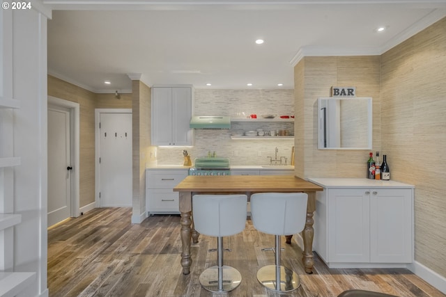 kitchen with sink, crown molding, wood-type flooring, a kitchen bar, and white cabinets