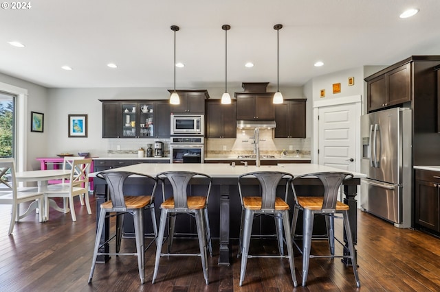 kitchen with hanging light fixtures, appliances with stainless steel finishes, and an island with sink