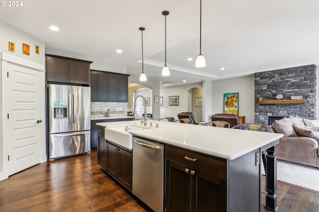 kitchen with dark brown cabinetry, stainless steel appliances, a kitchen island with sink, sink, and pendant lighting