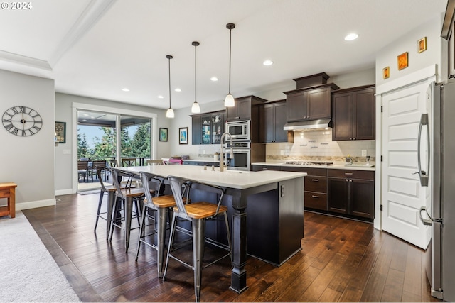 kitchen featuring dark brown cabinetry, stainless steel appliances, a kitchen island with sink, pendant lighting, and dark hardwood / wood-style floors