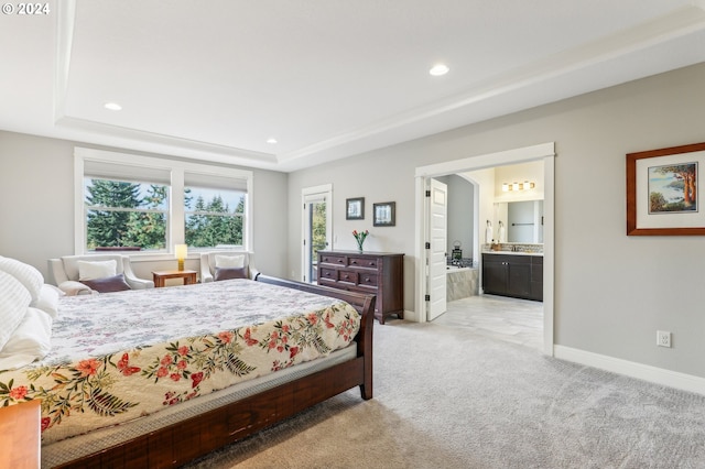 bedroom featuring a tray ceiling, ensuite bath, and light colored carpet