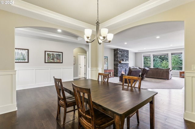 dining area with a stone fireplace, dark hardwood / wood-style flooring, crown molding, a chandelier, and a tray ceiling