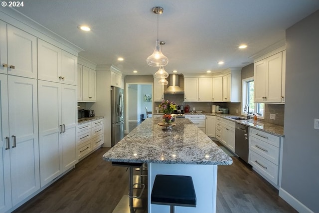 kitchen with white cabinets, appliances with stainless steel finishes, a center island, and wall chimney range hood