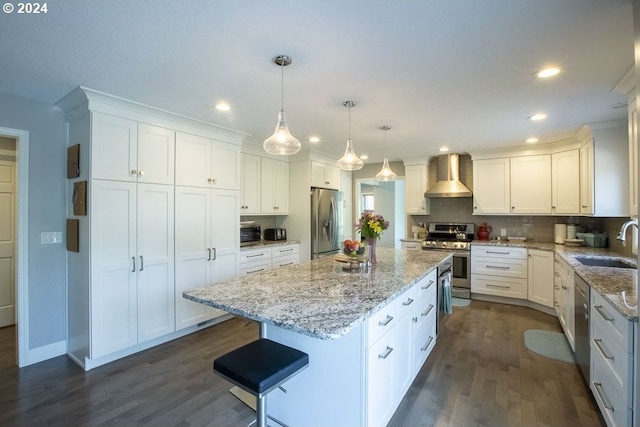 kitchen featuring sink, hanging light fixtures, appliances with stainless steel finishes, a kitchen island, and wall chimney range hood