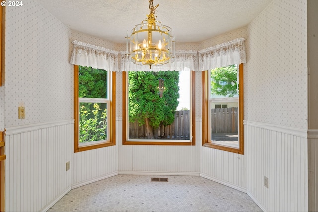 unfurnished room with an inviting chandelier, a wealth of natural light, carpet, and a textured ceiling