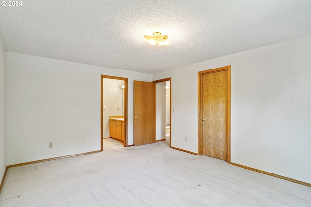 unfurnished bedroom featuring a textured ceiling, connected bathroom, and light colored carpet