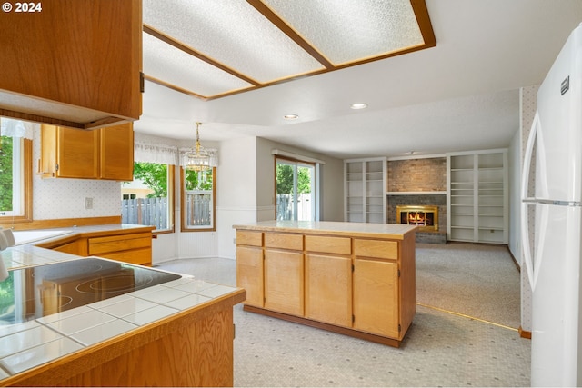 kitchen featuring white fridge, a fireplace, hanging light fixtures, tile countertops, and kitchen peninsula