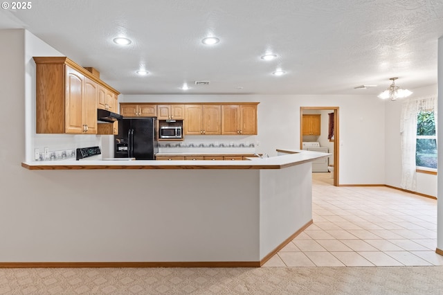 kitchen featuring black fridge, a notable chandelier, kitchen peninsula, washer / dryer, and light tile patterned floors