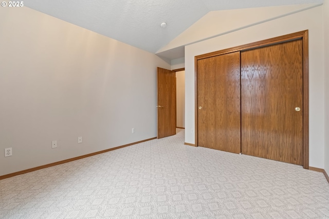 unfurnished bedroom featuring a textured ceiling, light colored carpet, vaulted ceiling, and a closet