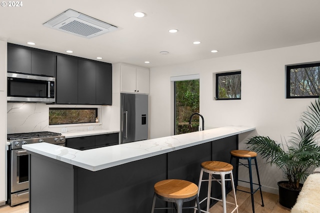 kitchen featuring appliances with stainless steel finishes, white cabinets, a kitchen bar, decorative backsplash, and kitchen peninsula