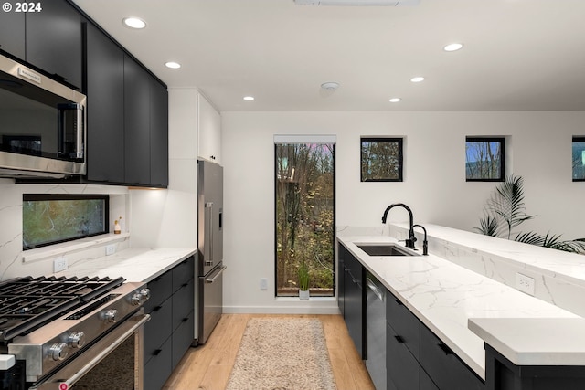 kitchen with sink, stainless steel appliances, light stone countertops, kitchen peninsula, and light wood-type flooring