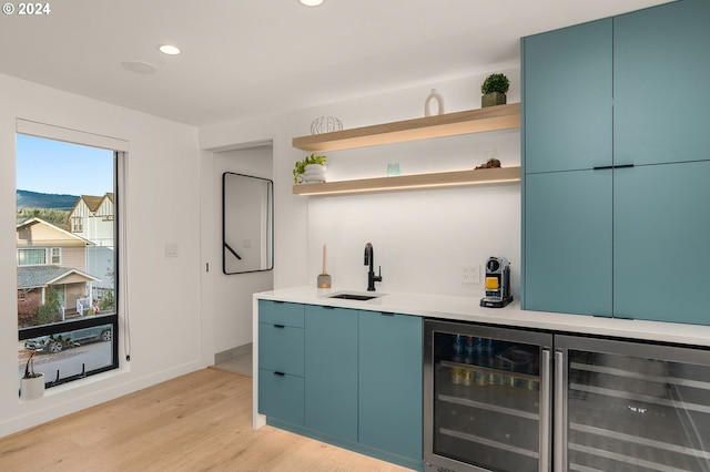 bar with blue cabinetry, sink, beverage cooler, and light wood-type flooring