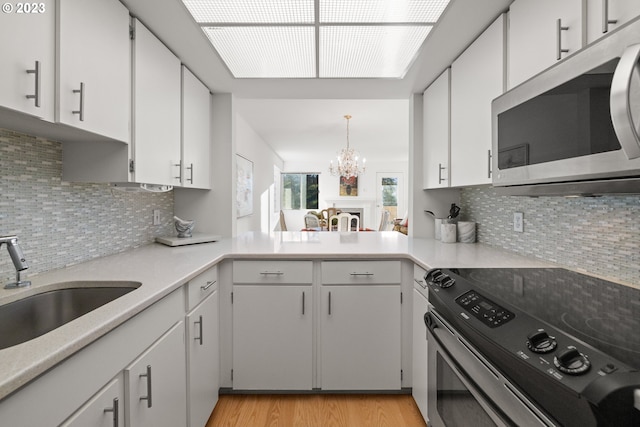 kitchen with appliances with stainless steel finishes, tasteful backsplash, a chandelier, and light hardwood / wood-style floors