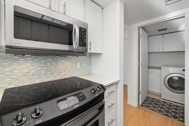 kitchen with black range oven, white cabinets, washer / dryer, and light wood-type flooring