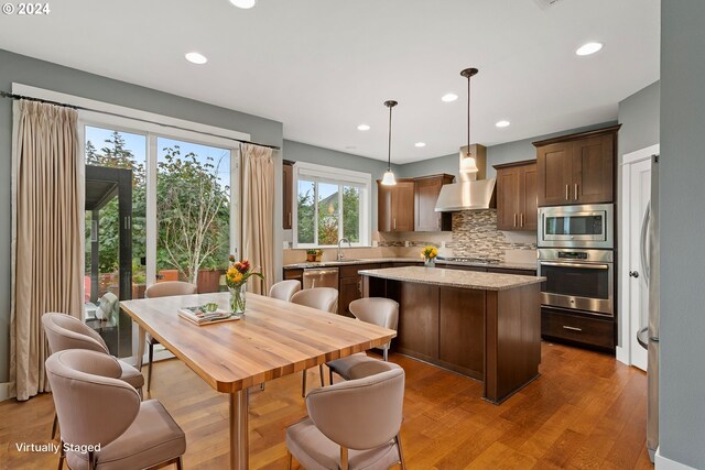 kitchen featuring pendant lighting, light hardwood / wood-style flooring, backsplash, stainless steel appliances, and a center island