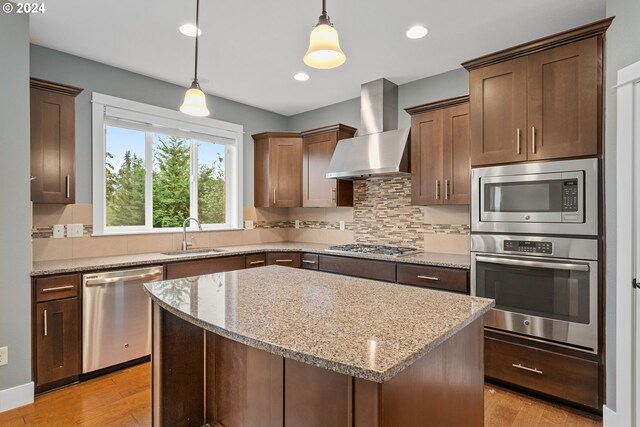 kitchen featuring a center island, wall chimney exhaust hood, sink, pendant lighting, and appliances with stainless steel finishes