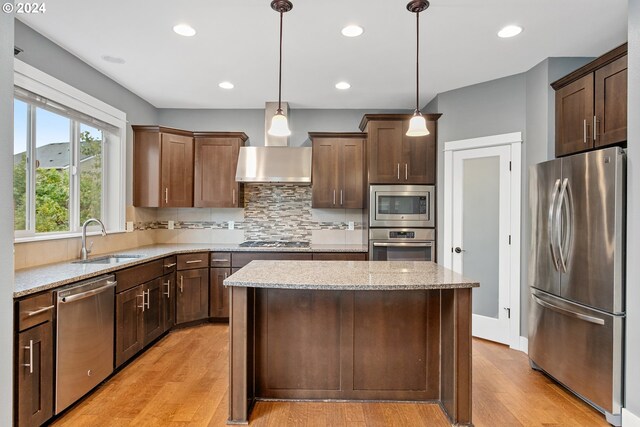 kitchen with a kitchen island, stainless steel appliances, sink, light hardwood / wood-style flooring, and decorative light fixtures