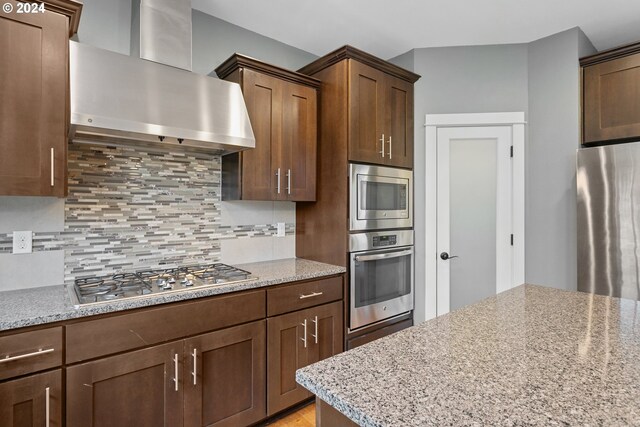 kitchen with appliances with stainless steel finishes, wall chimney exhaust hood, tasteful backsplash, and light stone countertops