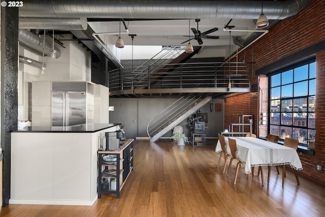 dining area featuring ceiling fan, hardwood / wood-style floors, a towering ceiling, and brick wall