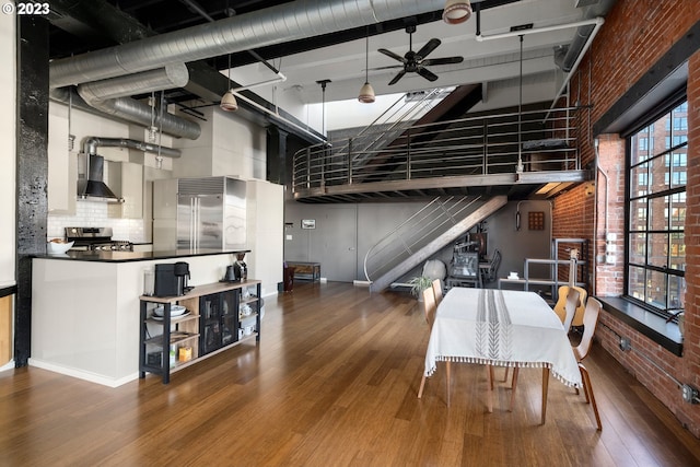 dining space with a towering ceiling, brick wall, ceiling fan, hardwood / wood-style flooring, and beamed ceiling