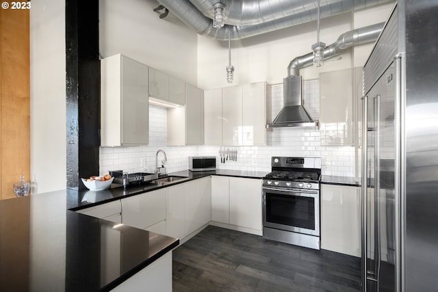 kitchen with wall chimney range hood, sink, appliances with stainless steel finishes, dark hardwood / wood-style flooring, and white cabinetry