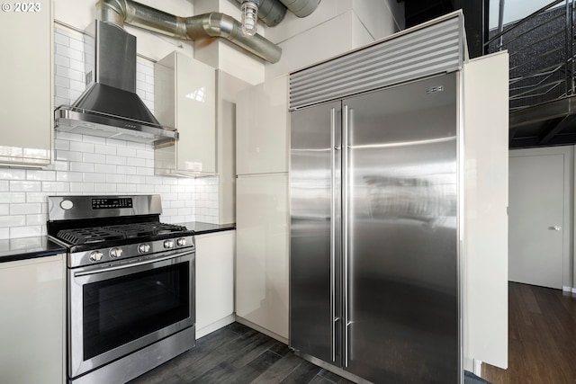 kitchen with appliances with stainless steel finishes, backsplash, wall chimney exhaust hood, dark wood-type flooring, and white cabinetry