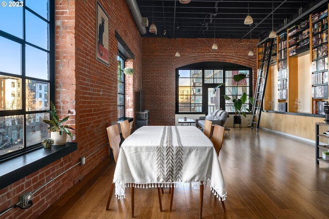 dining space with hardwood / wood-style flooring, brick wall, and a high ceiling