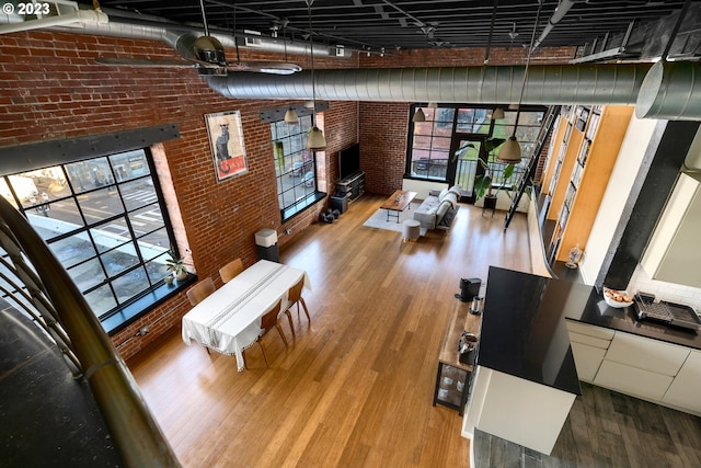 living room featuring a towering ceiling, wood-type flooring, and brick wall