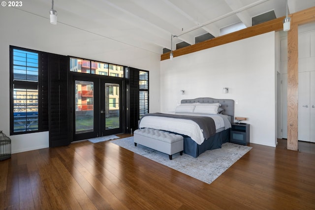 bedroom featuring beam ceiling, dark hardwood / wood-style flooring, access to outside, and a high ceiling