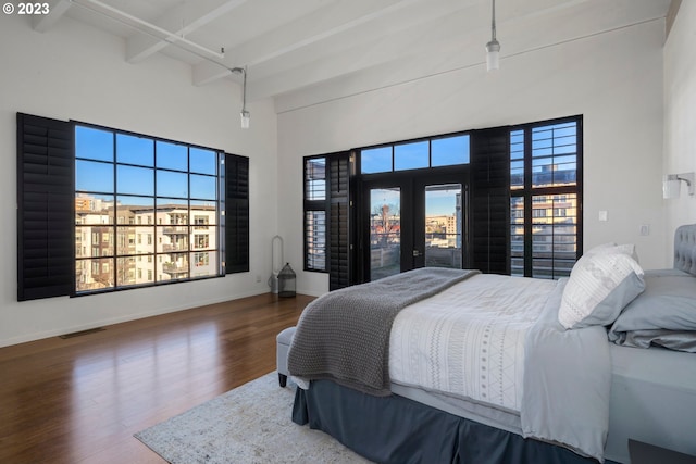 bedroom with hardwood / wood-style flooring, beam ceiling, a towering ceiling, and multiple windows