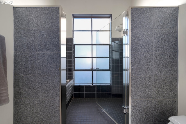 bathroom with toilet, tile patterned flooring, and tiled shower