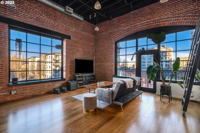 living room featuring hardwood / wood-style floors, a towering ceiling, and brick wall