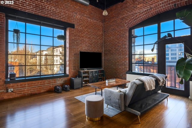 living room featuring hardwood / wood-style floors, a towering ceiling, and brick wall