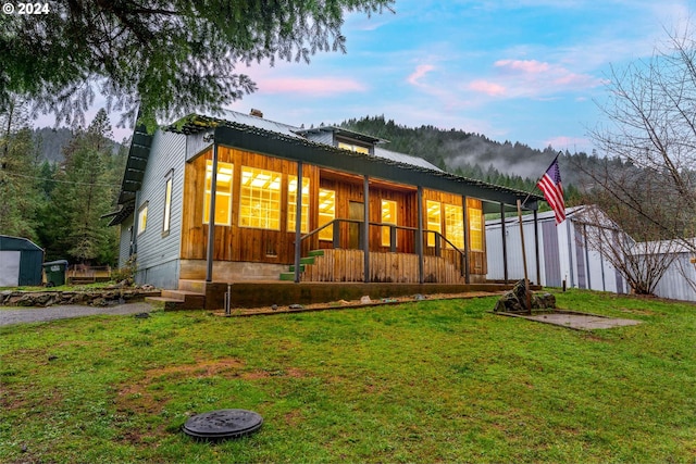 back house at dusk featuring a lawn, a storage unit, and a porch