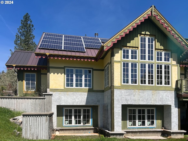 back of house with stucco siding, metal roof, and solar panels