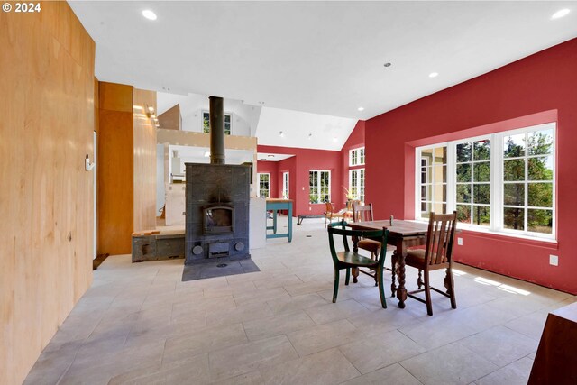 dining area featuring a wood stove, light tile patterned flooring, and lofted ceiling