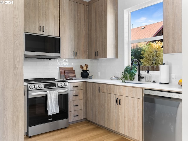 kitchen with light wood-type flooring, backsplash, sink, and stainless steel appliances