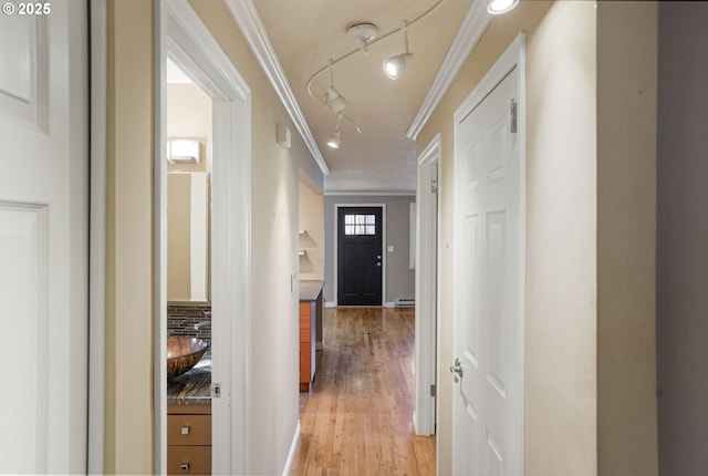 hallway with rail lighting, light hardwood / wood-style floors, a baseboard radiator, and ornamental molding