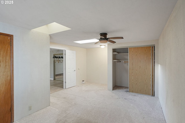 unfurnished bedroom featuring a skylight, a closet, light colored carpet, and ceiling fan