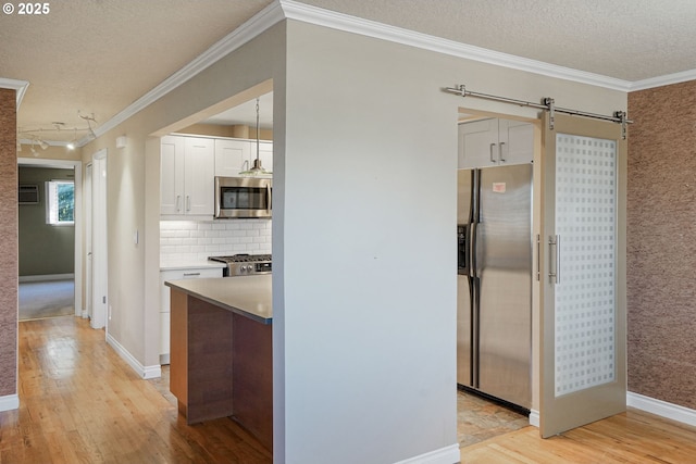 kitchen featuring stainless steel appliances, a barn door, crown molding, decorative backsplash, and white cabinets