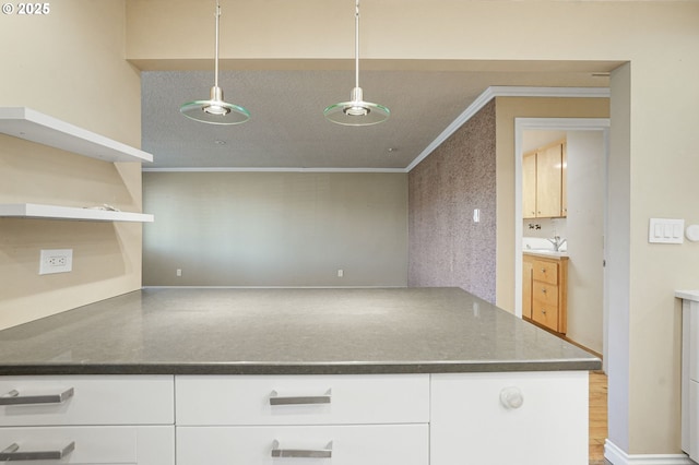 kitchen featuring white cabinets, kitchen peninsula, hanging light fixtures, and crown molding