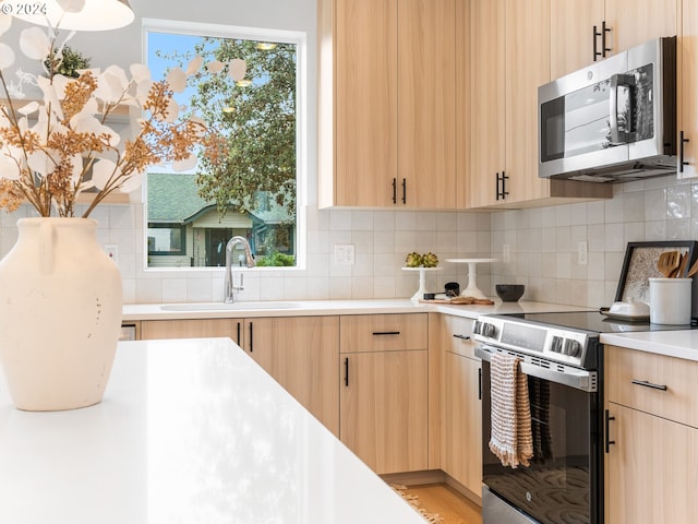 kitchen with hardwood / wood-style flooring, sink, appliances with stainless steel finishes, light brown cabinets, and decorative backsplash