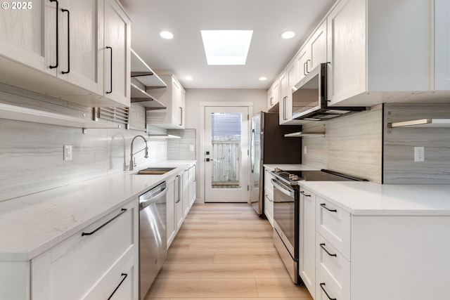 kitchen with backsplash, sink, a skylight, white cabinetry, and stainless steel appliances