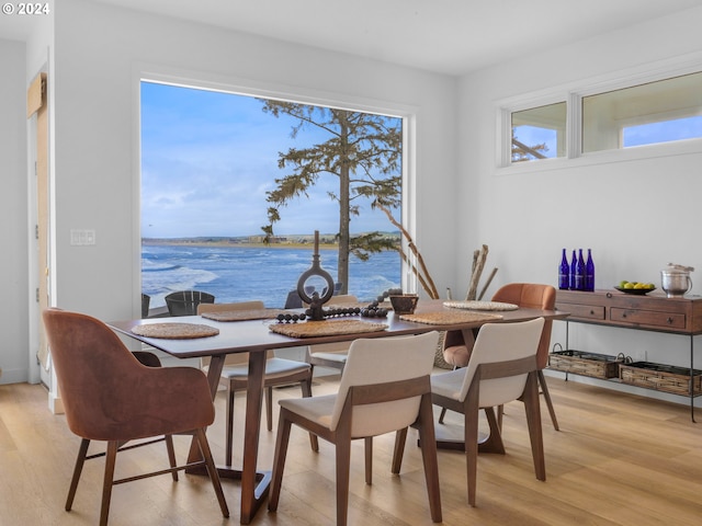 dining area with light hardwood / wood-style floors and a water view