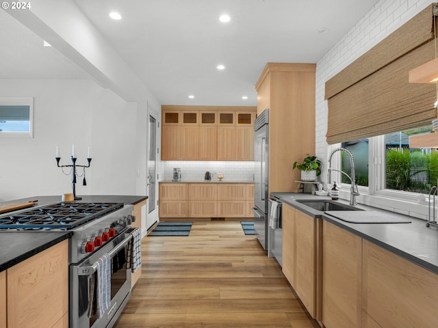 kitchen with light brown cabinets, sink, premium appliances, backsplash, and light wood-type flooring