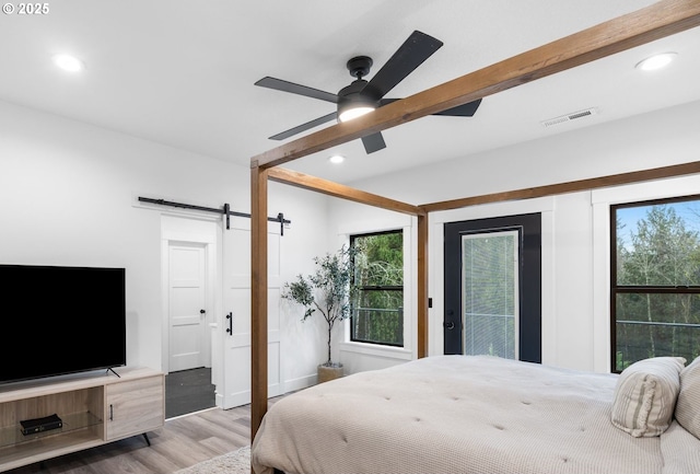 bedroom featuring wood finished floors, visible vents, a barn door, beamed ceiling, and multiple windows